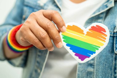 Gökkuşağı bilekliği takan Asyalı kadın ve kırmızı kalp, LGBT onur ayının sembolü, Haziran sosyal ortamında eşcinsel, lezbiyen, biseksüel, transseksüel, insan hakları kutlamaları.