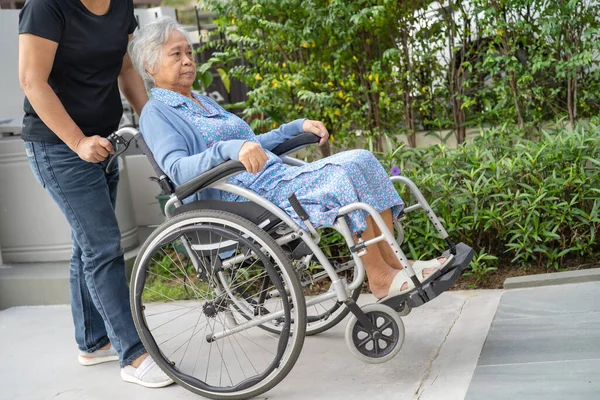 Caregiver help and care Asian senior woman patient sitting on wheelchair to ramp in nursing hospital, healthy strong medical concept.