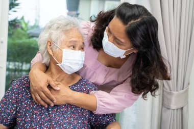 Tekerlekli sandalyedeki Asyalı yaşlı kadına yardım eden ve güvenlik enfeksiyonunu korumak için maske takan bakıcı Covid19 Coronavirus.