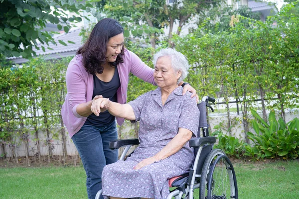 Caregiver help and care Asian senior woman patient sitting on wheelchair in park, healthy strong medical concept.