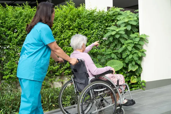 Caregiver help and care Asian senior woman patient sitting on wheelchair to ramp in hospital.