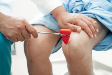 Asyalı doktor, hastanede diz reflekslerini, sinirlerini ve kaslarını kontrol etmek için çekici kullanıyor..