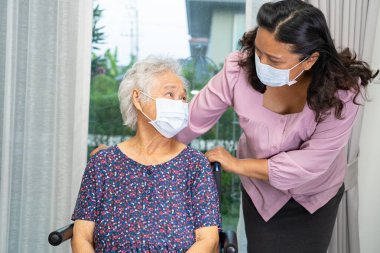 Tekerlekli sandalyedeki Asyalı yaşlı kadına yardım eden ve güvenlik enfeksiyonunu korumak için maske takan bakıcı Covid19 Coronavirus.