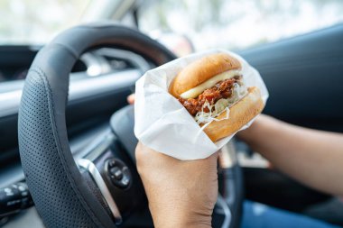 Arabada yemek için hamburger tutan Asyalı kadın tehlikeli ve kaza riski taşıyor..