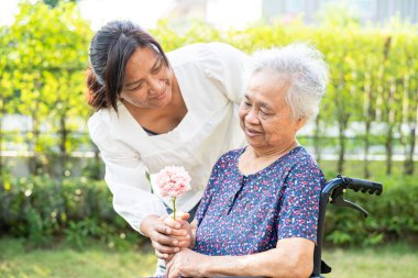 Caregive talk and help Asian elderly woman holding flower, smile and happy in the sunny garden.