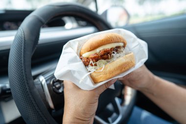 Arabada yemek için hamburger tutan Asyalı kadın tehlikeli ve kaza riski taşıyor..