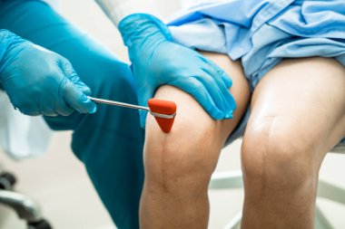 Asyalı doktor, hastanede diz reflekslerini, sinirlerini ve kaslarını kontrol etmek için çekici kullanıyor..