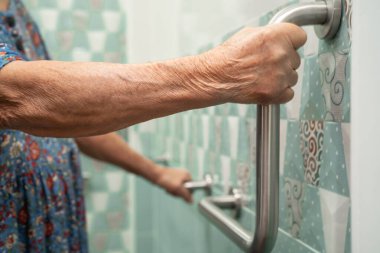 Asyalı yaşlı kadın tuvalette tuvalet tutacağı kullanıyor. Sağlıklı güçlü tıbbi konsept..