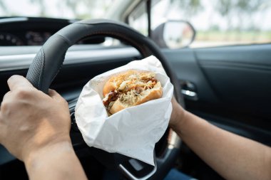 Arabada yemek için hamburger ve patates kızartması tutan Asyalı kadın tehlikeli ve kaza riski taşıyor..
