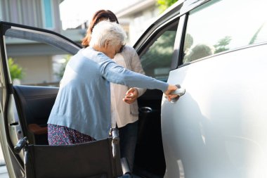 Caregiver help and support asian elderly woman sitting on wheelchair prepare get to her car to travel in holiday.