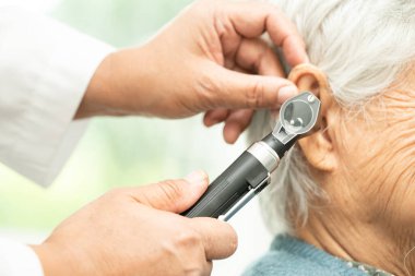 Odiyolog veya ENT doktoru otoskop kullanarak işitme sorunu olan Asyalı yaşlı kadın hastaların kulaklarını kontrol eder..