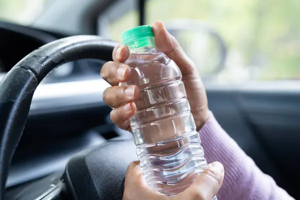 Asian woman driver holding bottle for drink water while driving a car. Plastic hot water bottle cause fire.