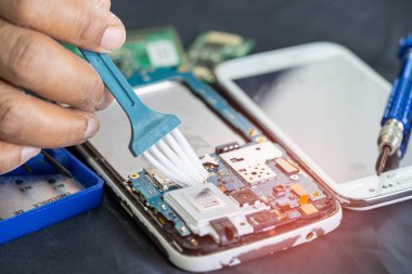 Asyalı teknisyen fırça, donanım, cep telefonu, güncelleme konsepti ile akıllı telefon elektronik teknolojisinin kirli mikro devre tamiri ve temizliği.