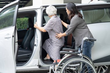 Caregiver help and support asian elderly woman sitting on wheelchair prepare get to her car to travel in holiday.