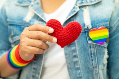 Gökkuşağı bilekliği takan Asyalı kadın ve kırmızı kalp, LGBT onur ayının sembolü, Haziran sosyal ortamında eşcinsel, lezbiyen, biseksüel, transseksüel, insan hakları kutlamaları.