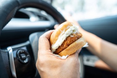 Arabada yemek için hamburger tutan Asyalı kadın tehlikeli ve kaza riski taşıyor..