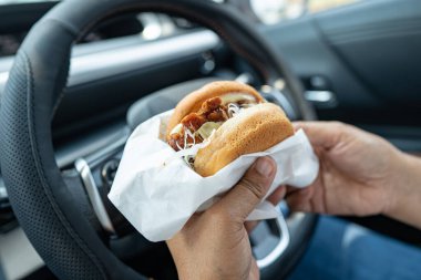 Arabada yemek için hamburger tutan Asyalı kadın tehlikeli ve kaza riski taşıyor..