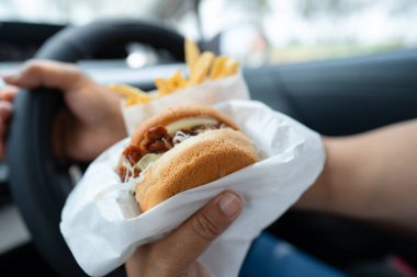 Arabada yemek için hamburger tutan Asyalı kadın tehlikeli ve kaza riski taşıyor..