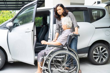 Caregiver help and support asian elderly woman sitting on wheelchair prepare get to her car to travel in holiday.