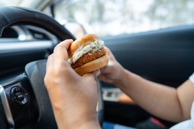 Arabada yemek için hamburger tutan Asyalı kadın tehlikeli ve kaza riski taşıyor..