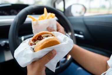 Arabada yemek için hamburger tutan Asyalı kadın tehlikeli ve kaza riski taşıyor..