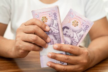 Asyalı iş kadını Tayland banknotlarını elinde tutuyor..