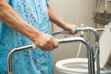 Asyalı yaşlı kadın hasta yürüteç ve tuvalet kullanıyormuş. Hemşirelik hastanesinde güvenlik sağlıyormuş. Sağlıklı, güçlü bir tıbbi tedavi..