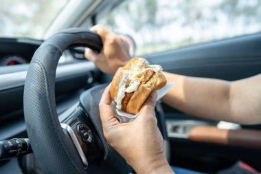 Arabada yemek için hamburger tutan Asyalı kadın tehlikeli ve kaza riski taşıyor..