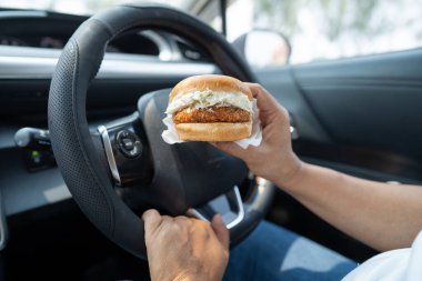 Arabada yemek için hamburger tutan Asyalı kadın tehlikeli ve kaza riski taşıyor..