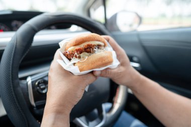 Arabada yemek için hamburger tutan Asyalı kadın tehlikeli ve kaza riski taşıyor..