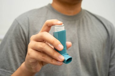 Astım ve kronik obstrüktif akciğer hastalığı COPD, Asyalı genç adam ölçülü doz solunum cihazı kullanıyor..