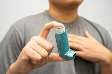 Astım ve kronik obstrüktif akciğer hastalığı COPD, Asyalı genç adam ölçülü doz solunum cihazı kullanıyor..