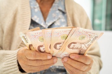 Tayland 'da elinde para tutan Asyalı yaşlı bir kadın. Yoksulluk, emeklilikte tasarruf sorunu.