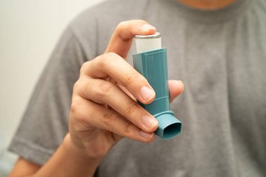 Astım ve kronik obstrüktif akciğer hastalığı COPD, Asyalı genç adam ölçülü doz solunum cihazı kullanıyor..