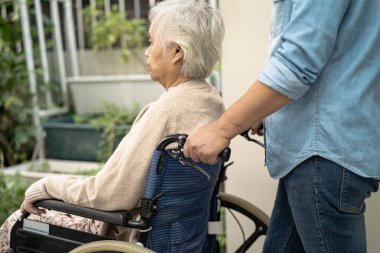 Bakıcı yardım ve bakım Asyalı yaşlı kadın hasta tekerlekli sandalyede hemşirelik hastanesinde rampaya oturuyor, sağlıklı ve güçlü bir tıbbi tedavi..
