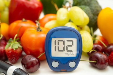 Asya 'da el ele tutuşan dijital glikoz monitörü sebze ve meyveli sağlıklı gıda ölçümü.