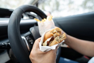 Arabada yemek için hamburger tutan Asyalı kadın tehlikeli ve kaza riski taşıyor..