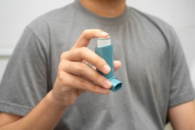 Astım ve kronik obstrüktif akciğer hastalığı COPD, Asyalı genç adam ölçülü doz solunum cihazı kullanıyor..