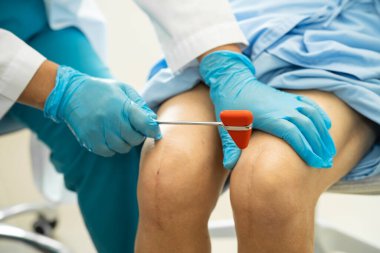 Ortopedi kliniğinde kıdemli bir hastanın diz ve bacağını muayene eden Asyalı doktor fizyoterapisti..