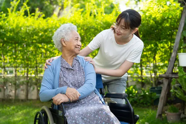 Bakıcı yardım ve bakım Asyalı yaşlı kadın hasta hemşire hastanesi koğuşunda tekerlekli sandalyede oturuyor, sağlıklı ve güçlü..