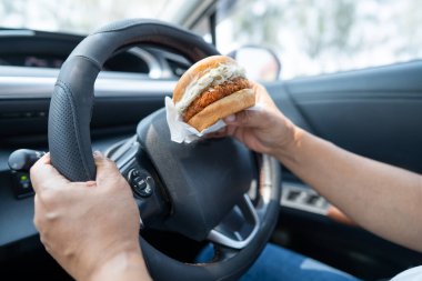 Arabada yemek için hamburger tutan Asyalı kadın tehlikeli ve kaza riski taşıyor..