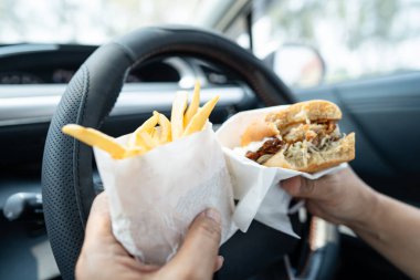 Arabada yemek için hamburger tutan Asyalı kadın tehlikeli ve kaza riski taşıyor..
