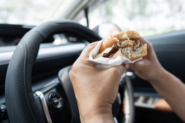Arabada yemek için hamburger tutan Asyalı kadın tehlikeli ve kaza riski taşıyor..