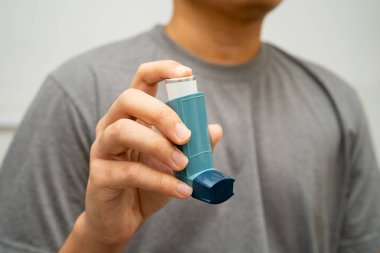 Astım ve kronik obstrüktif akciğer hastalığı COPD, Asyalı genç adam ölçülü doz solunum cihazı kullanıyor..