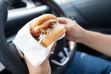 Arabada yemek için hamburger tutan Asyalı kadın tehlikeli ve kaza riski taşıyor..