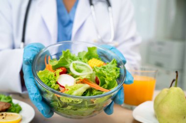Beslenme uzmanı doktor hasta için çeşitli sağlıklı sebzeler tutuyor..
