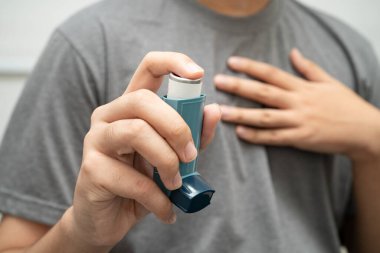 Astım ve kronik obstrüktif akciğer hastalığı COPD, Asyalı genç adam ölçülü doz solunum cihazı kullanıyor..
