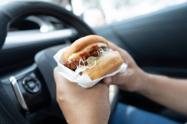 Arabada yemek için hamburger tutan Asyalı kadın tehlikeli ve kaza riski taşıyor..