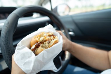 Arabada yemek için hamburger tutan Asyalı kadın tehlikeli ve kaza riski taşıyor..