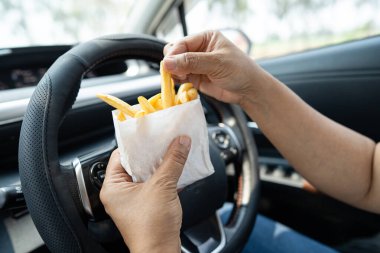 Arabada yemek için patates cipsi tutan Asyalı kadın tehlikeli ve kaza riski taşıyor..
